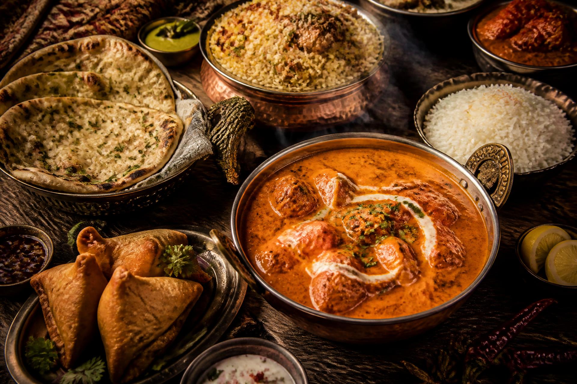 A spread of butter chicken, biryani, garlic naan and samosas on a rustic table